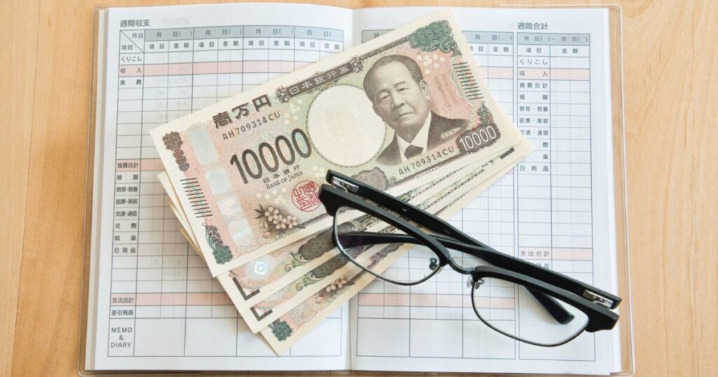 一万円札とメガネと家計簿の家計管理イメージ